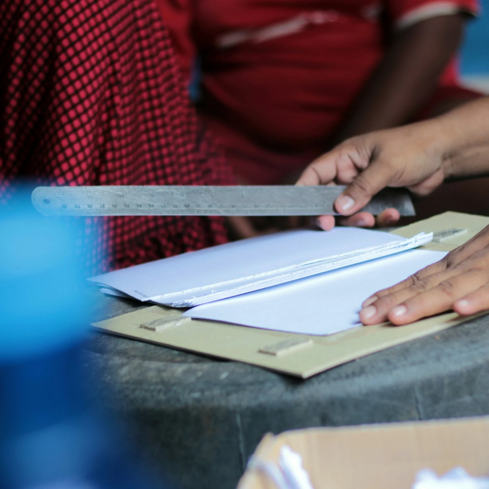 A person's hands use a metal ruler to align a stack of paper on a table.