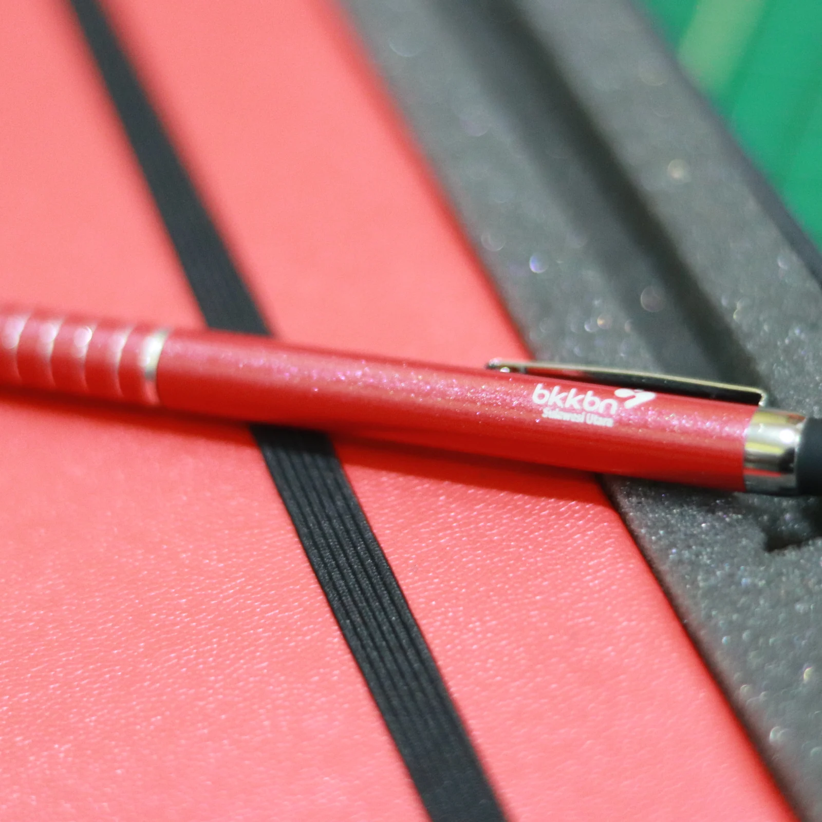 A red stylus pen with a bkkbn logo placed on a red surface.