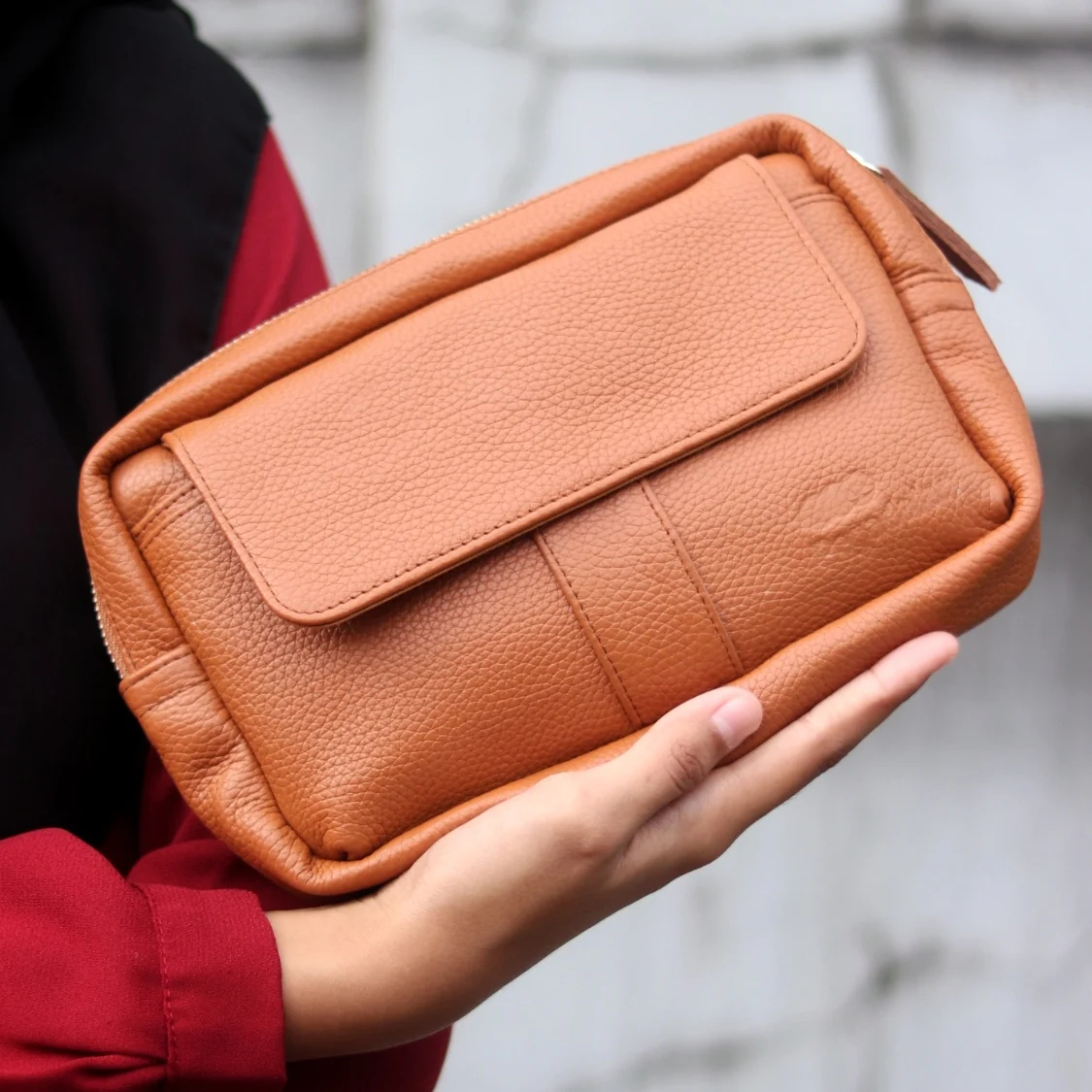 A person holding a brown leather pouch with a Pegadaian logo embossed on the surface.