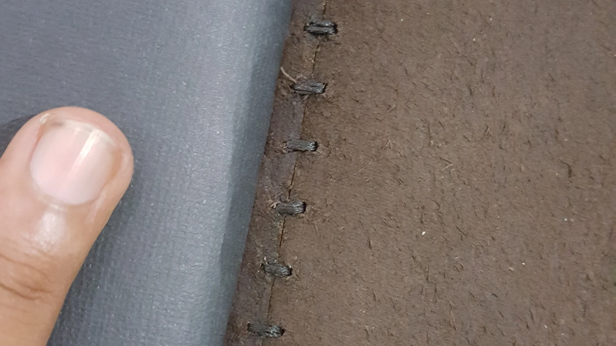A hand holding the spine of a leather journal, closely sewn by hand
