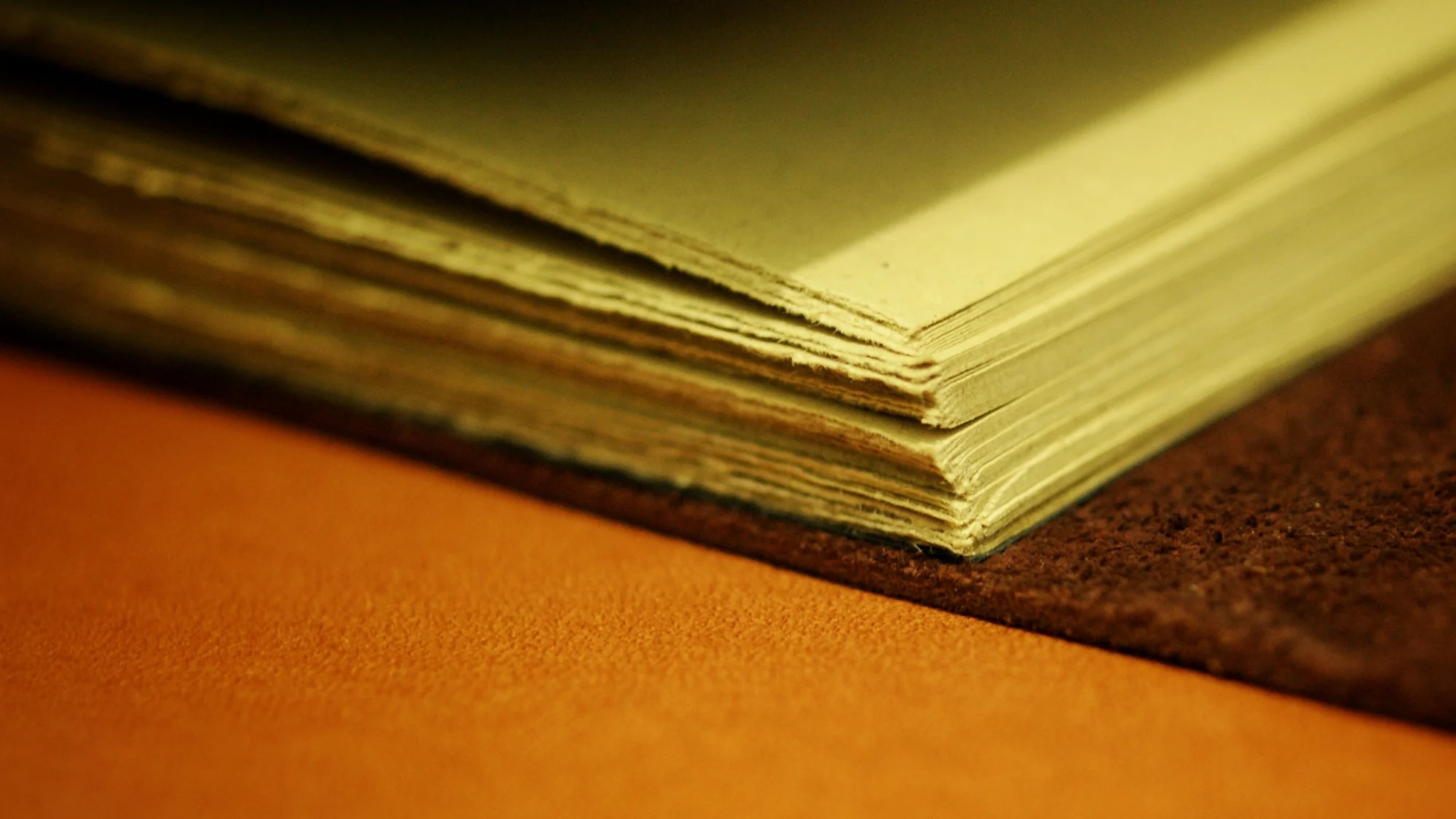 Close detail of paper edges and a suede leather cover in warm light
