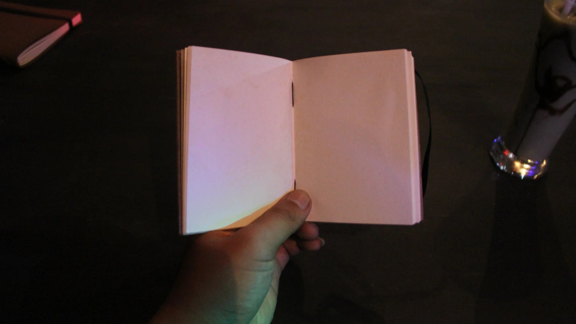 Sebuah tangan memegang buku catatan terbuka berhalaman kosong