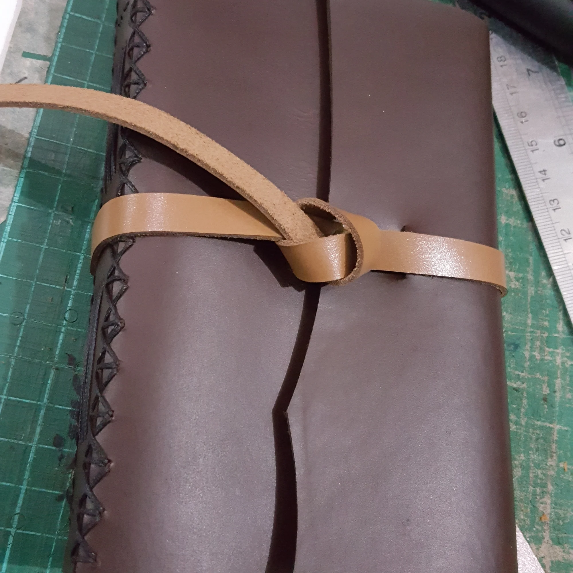 A brown leather journal with a tie strap on a cutting mat