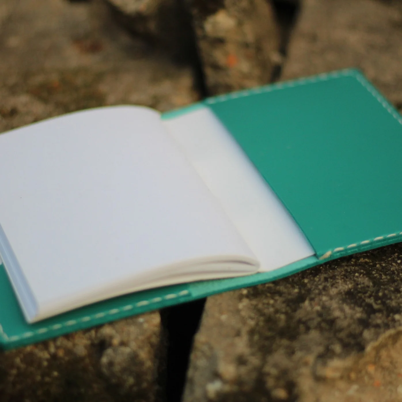A teal leather journal with a flap slip design placed on a stone surface.