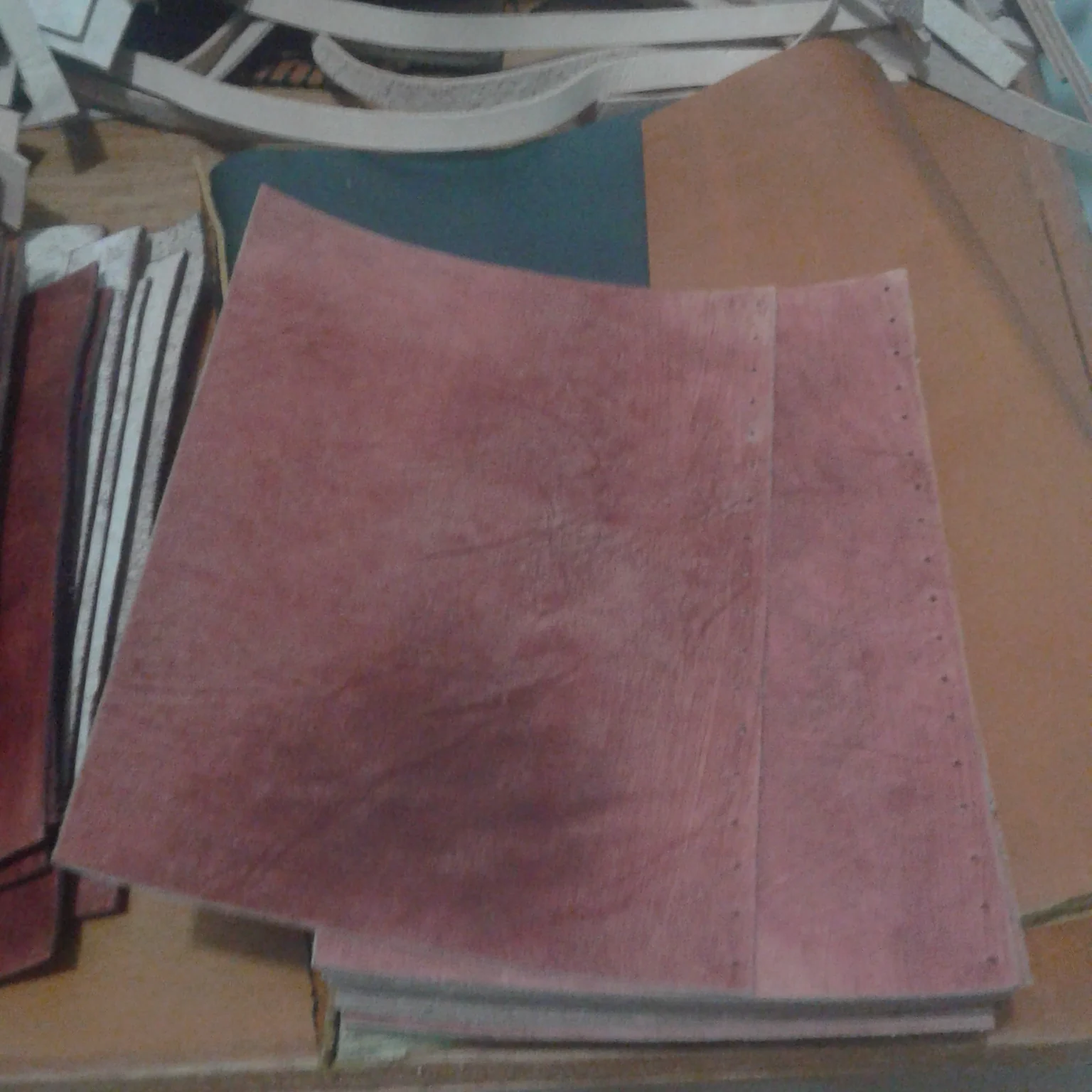Pink leather pieces with pre-punched stitching holes on a workbench.