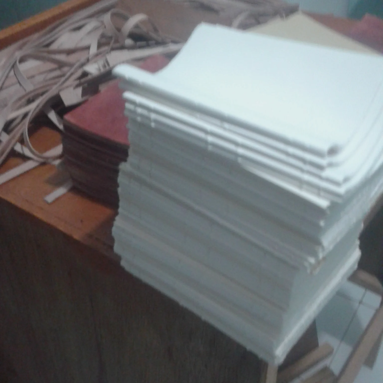 A stack of white paper signatures placed on a wooden table in a workshop.