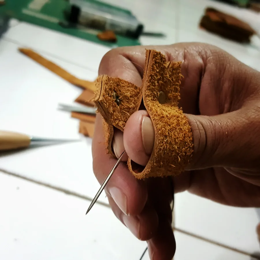 A hand wearing a leather finger guard, holding a sewing needle