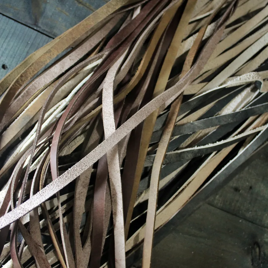 A pile of long leather offcuts on a wooden surface