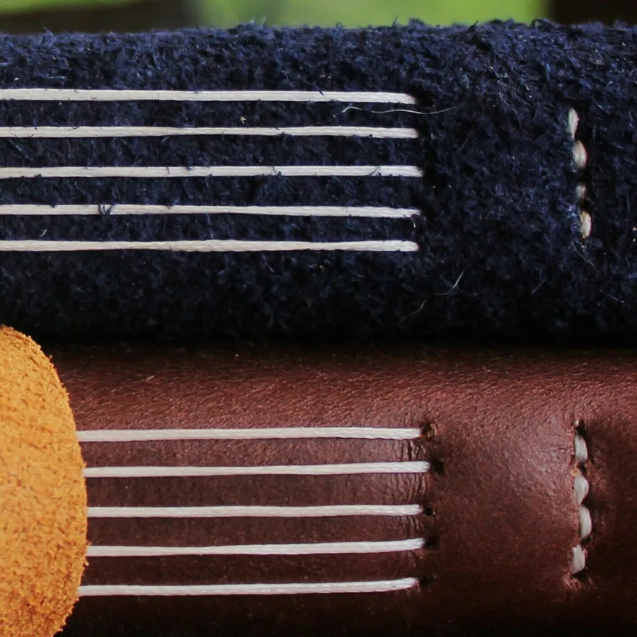 The spines of two leather journals close up, showing neat white stitching