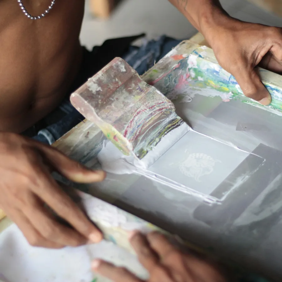 Two hands drawing a squeegee across a screen-printing frame