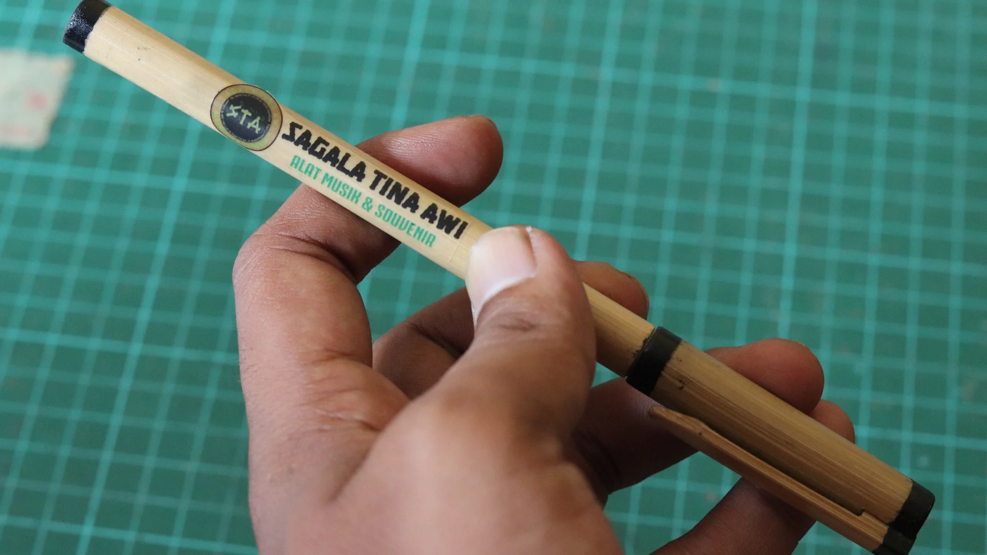 Tangan memegang pena bambu dengan logo Sagala Tina Awi