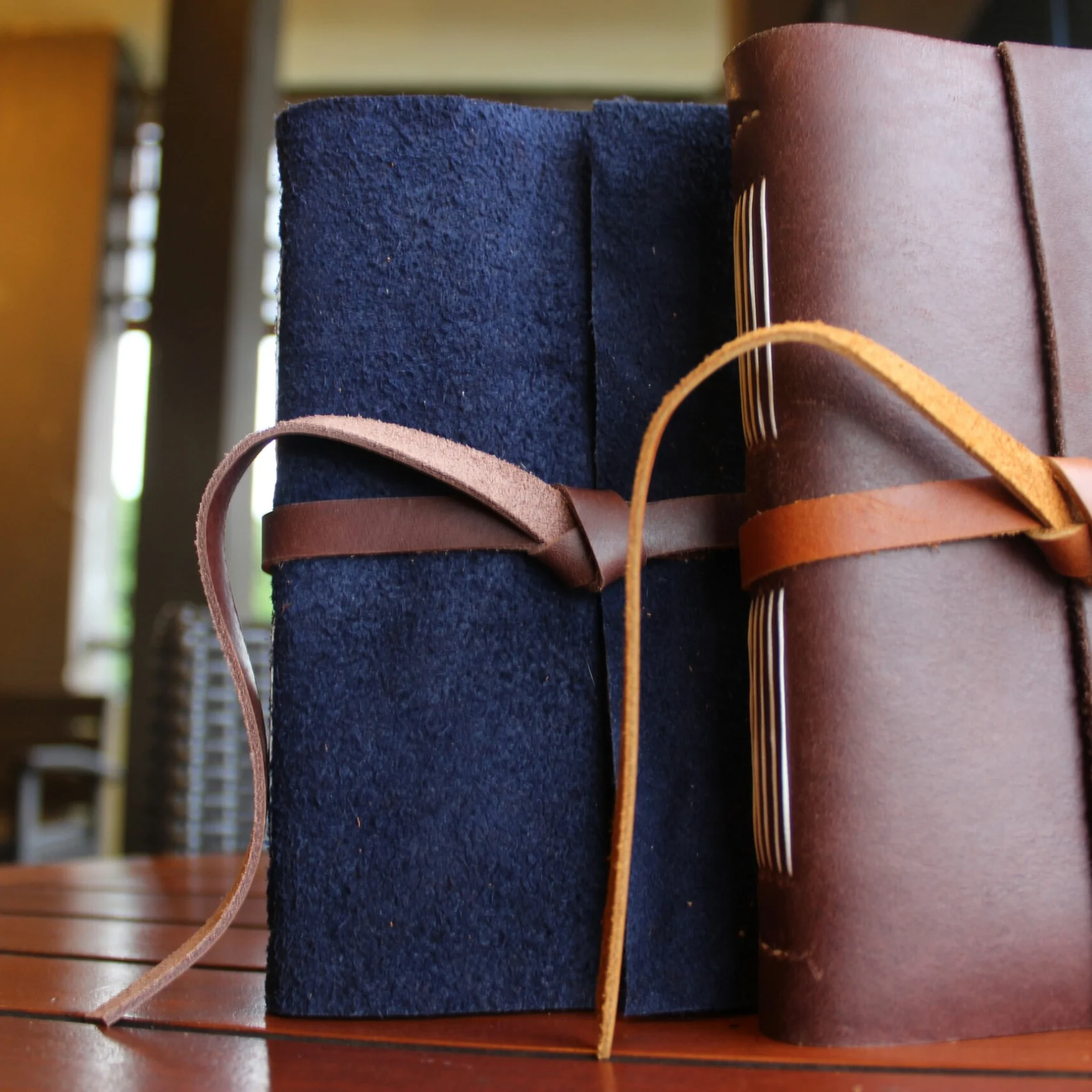 Two leather journals with wrap ties on a wooden table.