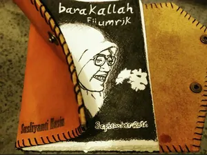 Sampul kulit dengan potret seorang perempuan berkacamata digambar tangan, bertuliskan barakallah fii umrik dan September 2016