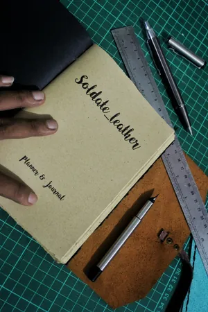 Sampul jurnal kertas kraft bertuliskan tangan Soldate_leather, Planner & Journal, di atas matras potong hijau bersama penggaris baja dan dua pena teknis