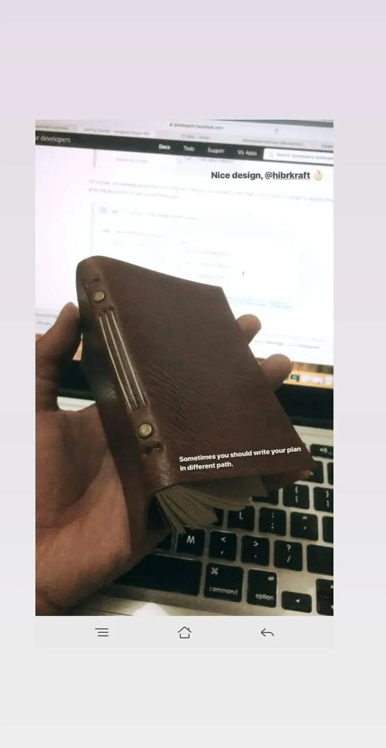 Story Instagram: tangan memegang jurnal kulit cokelat di atas laptop, dengan komentar Nice design