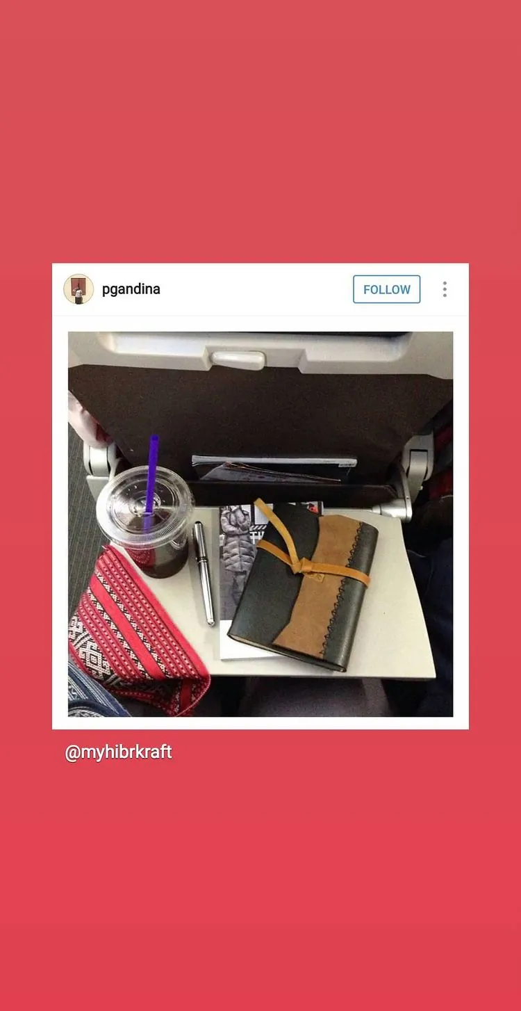 Story Instagram dari @pgandina: jurnal kulit, pouch batik dan es kopi di atas meja lipat pesawat