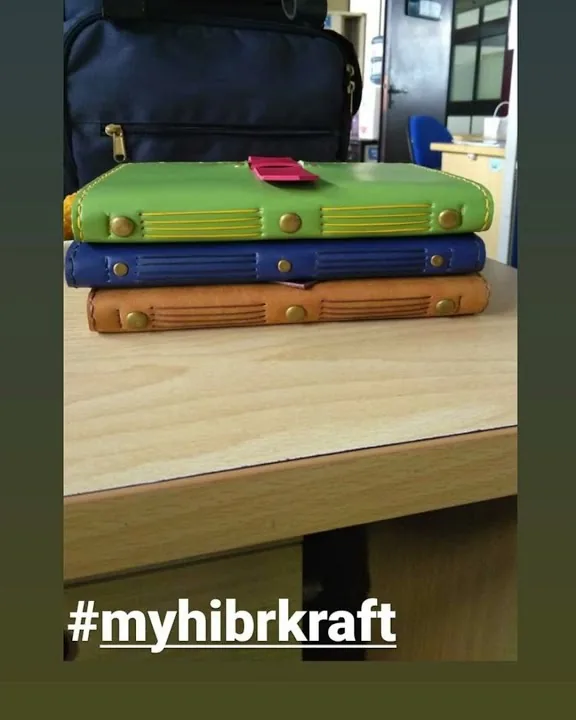 Tiga jurnal kulit hijau, biru dan tan ditumpuk di atas meja kayu