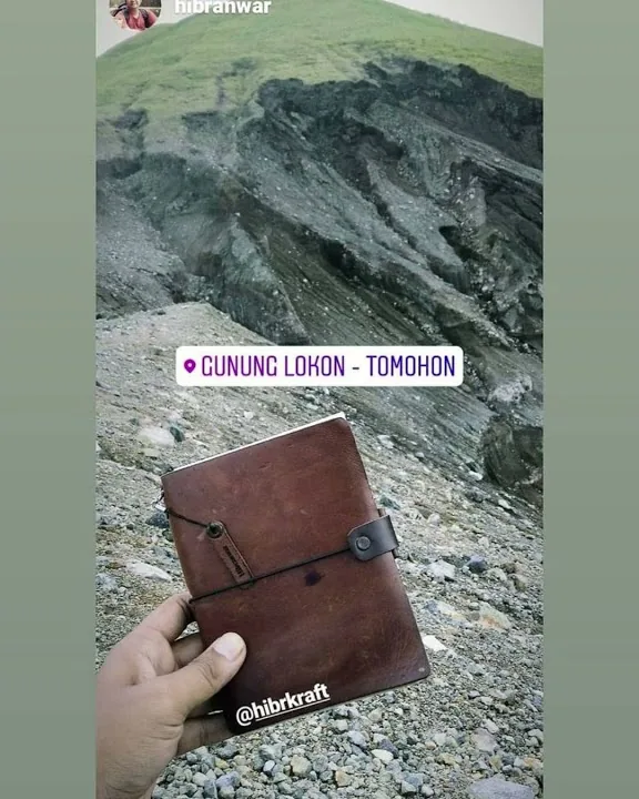 Jurnal kulit cokelat dipegang di atas kawah berbatu Gunung Lokon