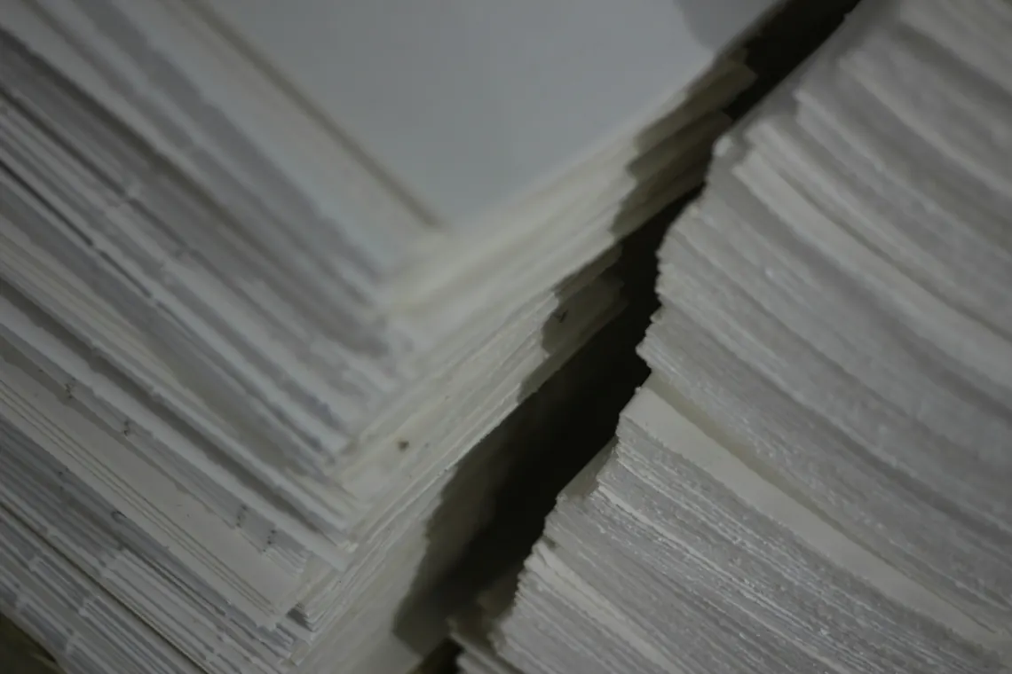 Lembar kertas putih ditumpuk rapi di bengkel sebelum dipotong.