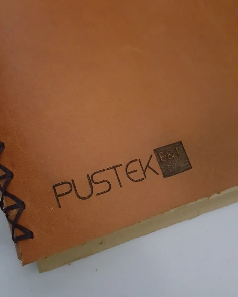 A leather journal cover with the Pustek ET logo debossed