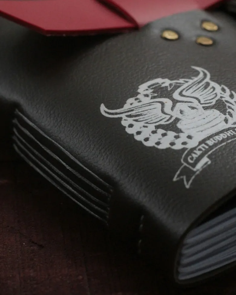 A black leather journal with the Cakti Buddhi Bhakti logo