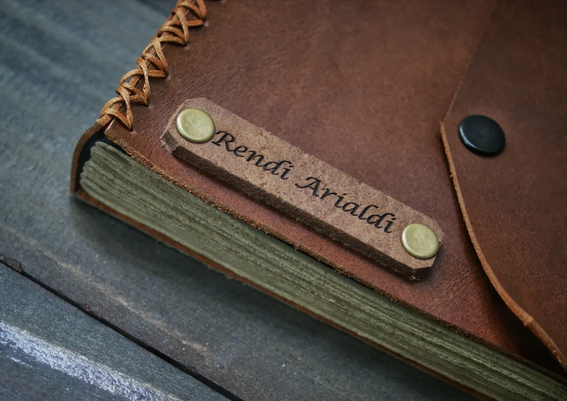 Detail label nama Rendi Arialdi terpasang pada sampul jurnal kulit.