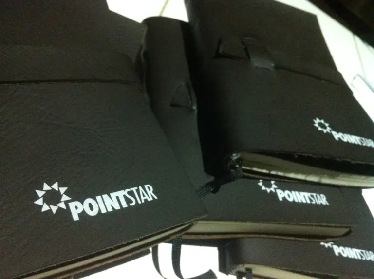 Tumpukan jurnal kulit hitam identik dengan logo Pointstar dideboss di sampul depan setiap eksemplar