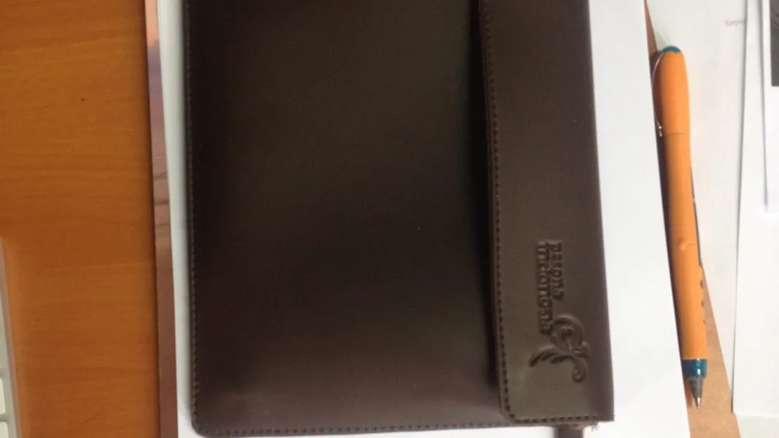 A brown leather portfolio with a company logo debossed on the cover.