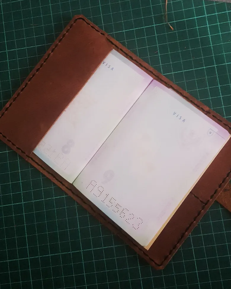 A leather passport holder with hand stitching along its edge.
