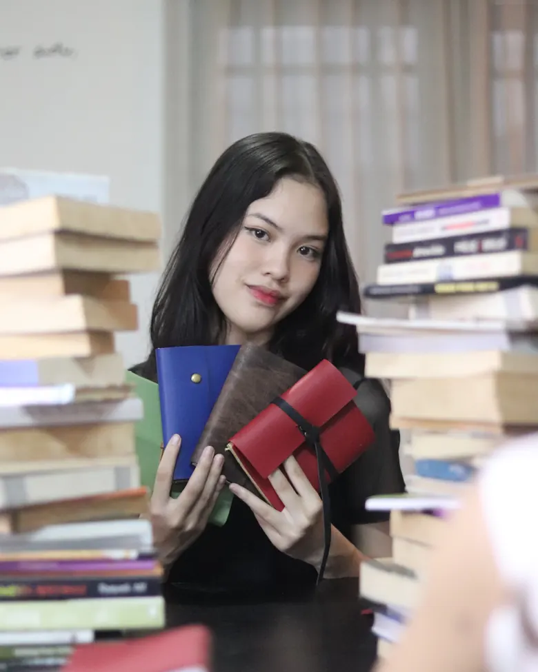 Seseorang memegang tiga jurnal kulit yang disusun berjajar.