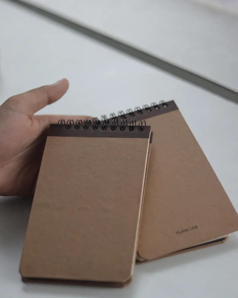 Tangan memegang dua buku catatan spiral bersampul kraft