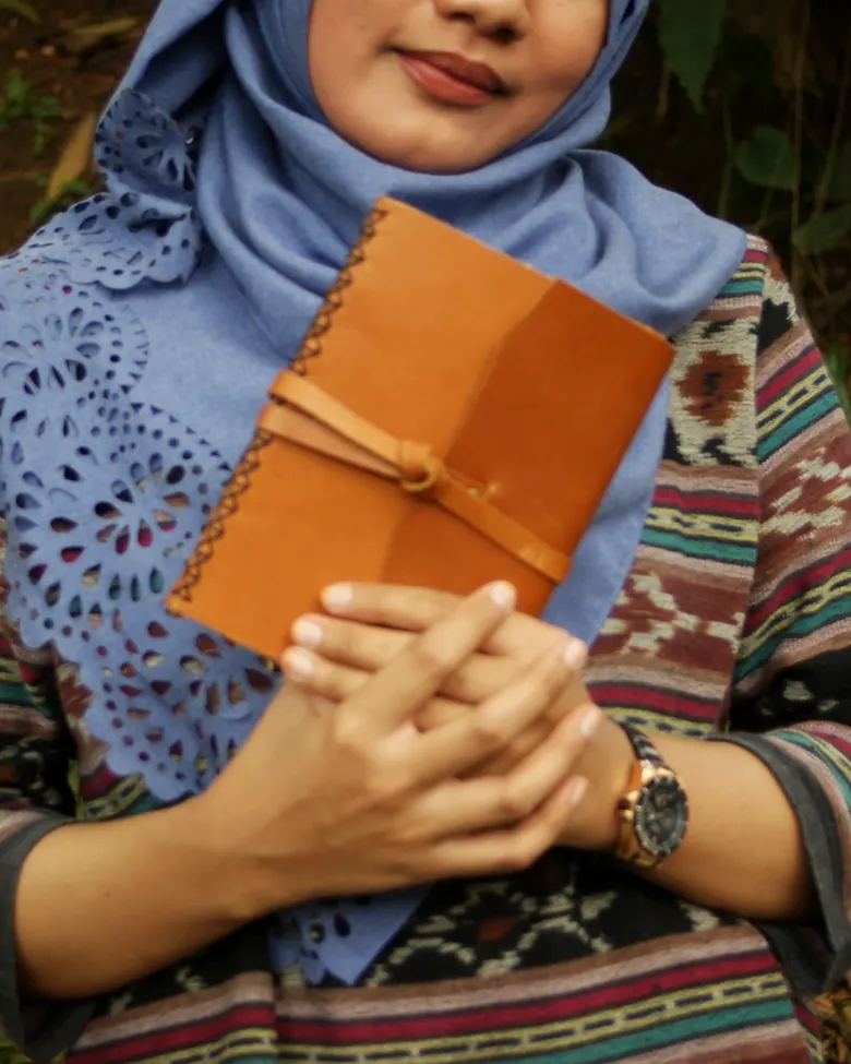Seorang perempuan memegang jurnal kulit cokelat muda dengan kedua tangan