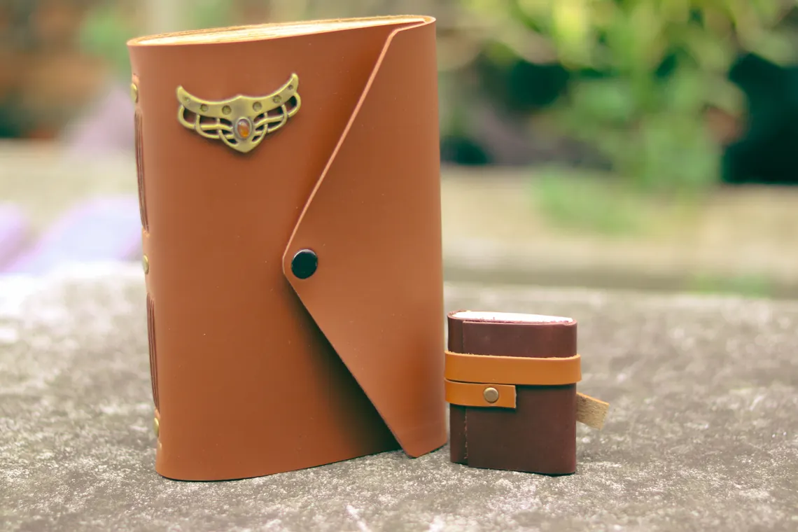 Jurnal kulit model Firhan dengan lambang logam pada sampul.