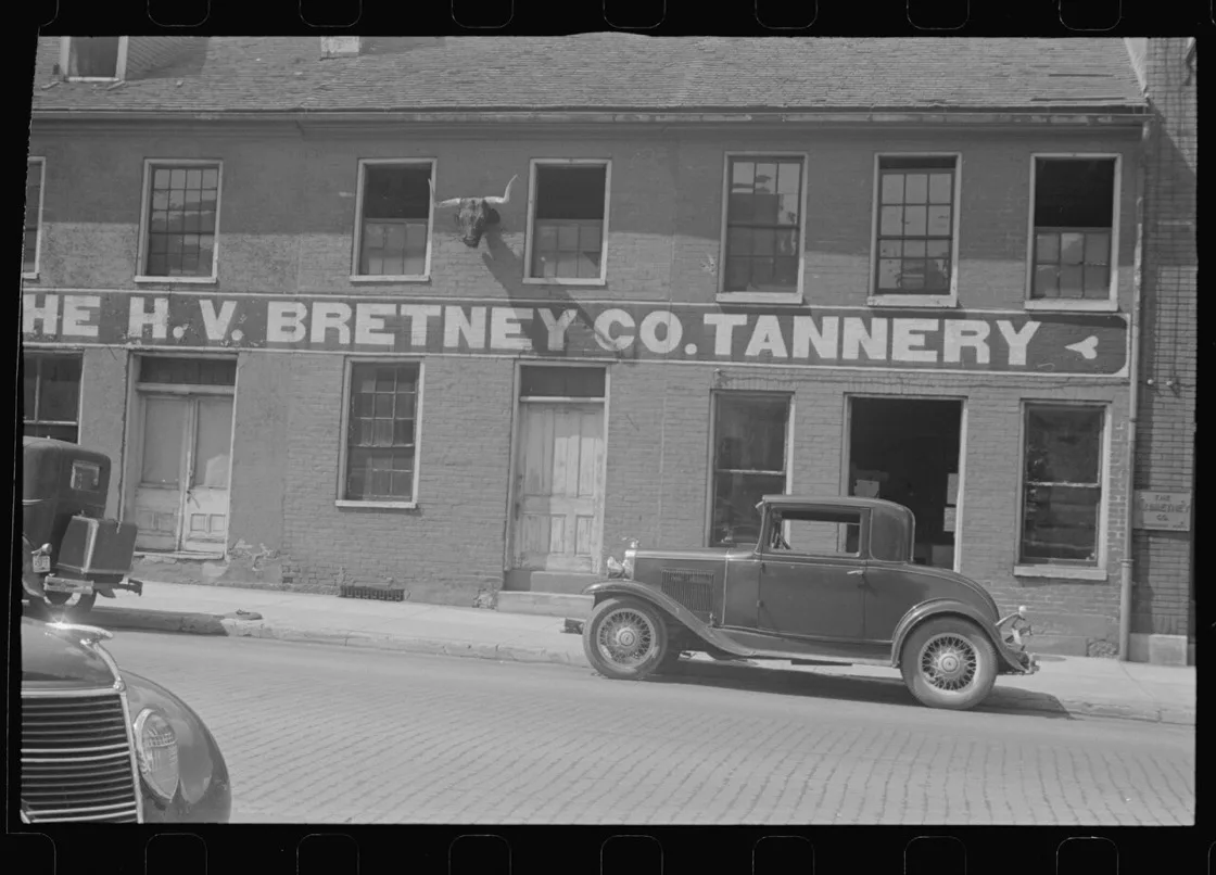 Fasad bangunan H.V. Bretney Co. Tannery di Springfield, Ohio, tahun 1938, dengan tanduk sapi terpasang di atas papan nama dan mobil bergaya 1930-an terparkir di tepi jalan berbatu