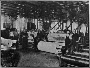 COATING ROOM, APPLETON COATED PAPER CO. This view of the “wet end” of the coating machines shows the rolls going through the coating process, the web of paper traveling along the drying racks appears in the background.