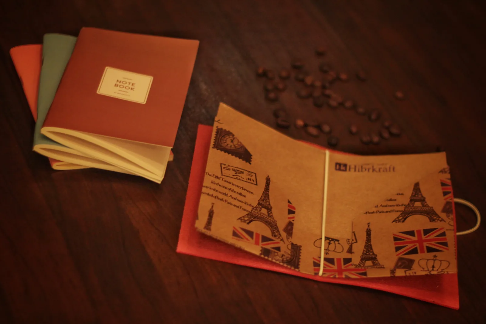 Uma capa de papel kraft impressa com a Torre Eiffel, uma bandeira do Reino Unido e marcas postais, carimbada Hk Hibrkraft, com miolos de caderno e grãos de café à volta