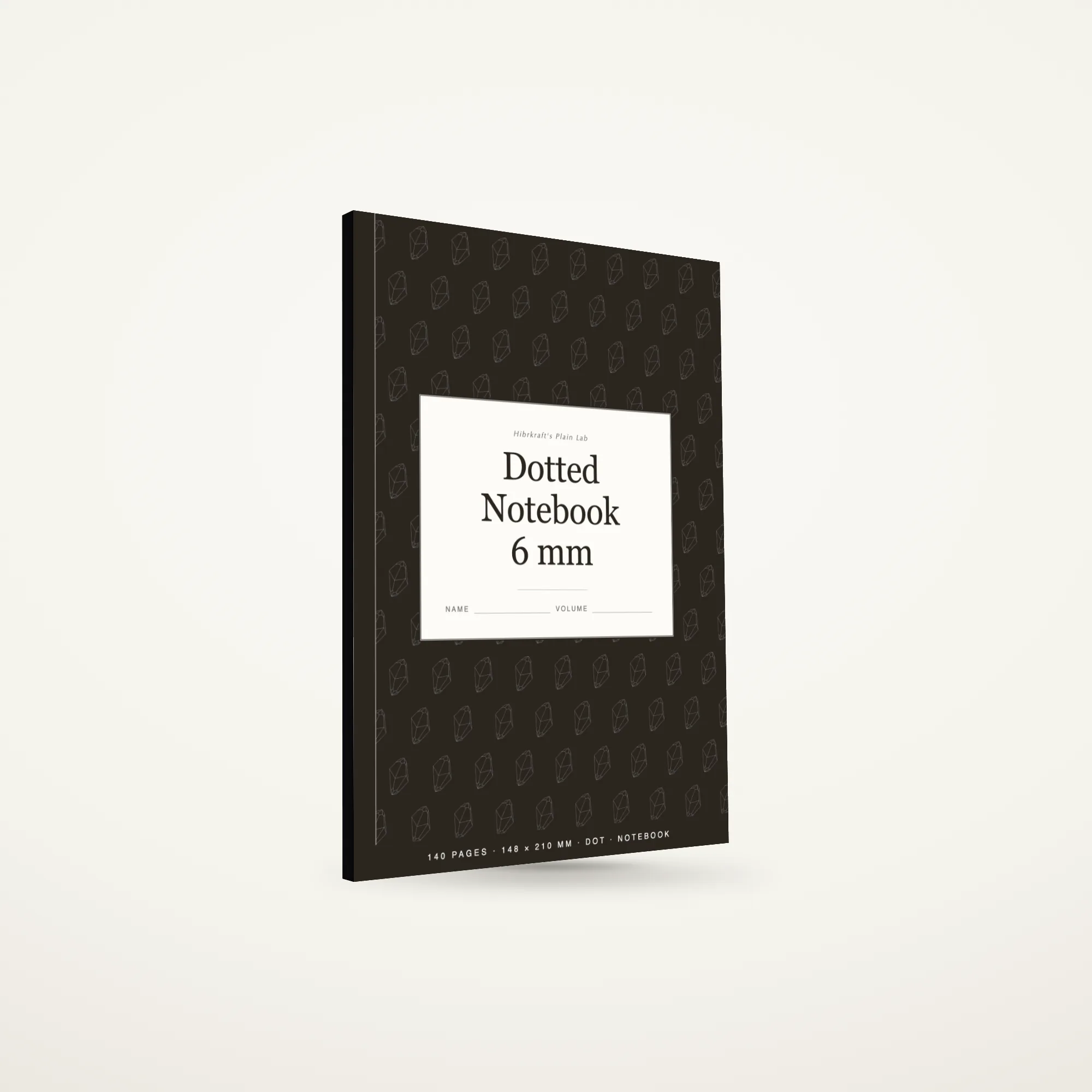 A5 dotted notebook standing closed on a plain surface, composition-style cover with a tiled illustration field and a label plate, about eight millimetres thick.