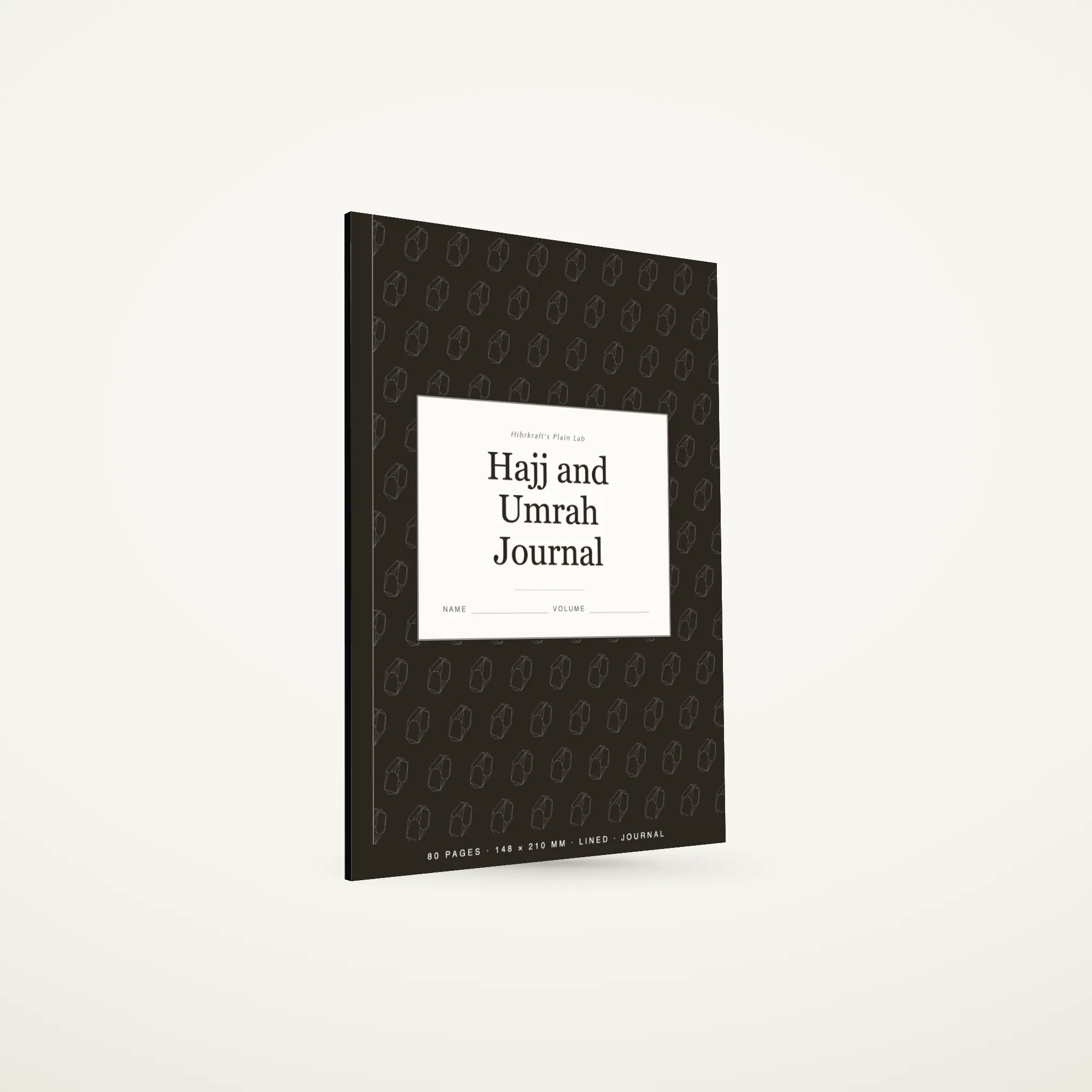Closed a5 Hajj and Umrah Journal standing on a plain surface, a tiled illustration field on the cover, a cream label plate near the middle, a narrow binding strip down the spine.